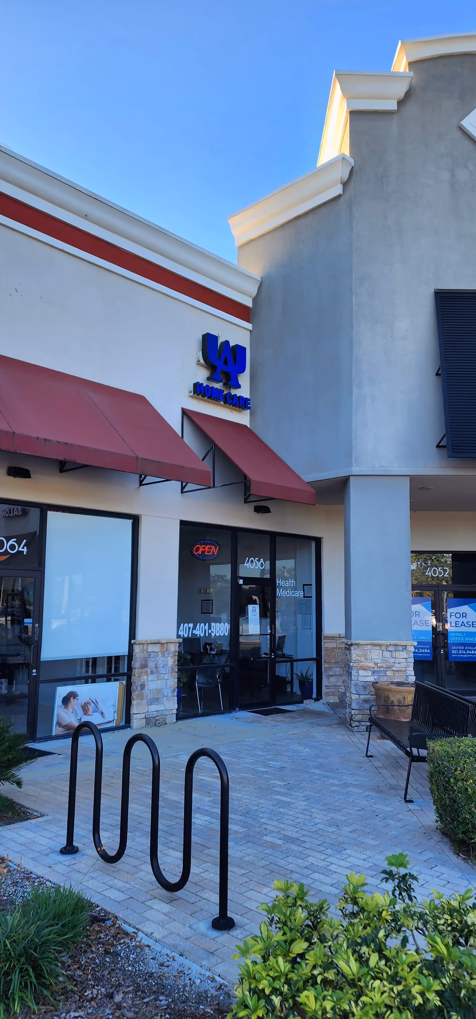 Front exterior of a strip mall storefront with red awnings and a blue sign.