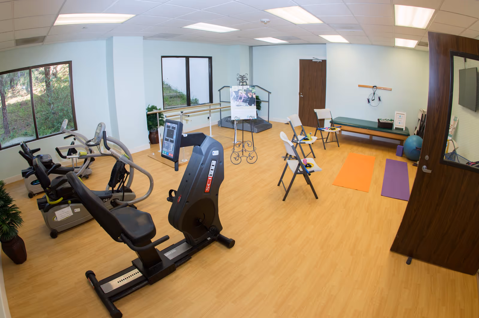 Interior fitness room with cardio machines, mats, and a bench in a senior living facility.