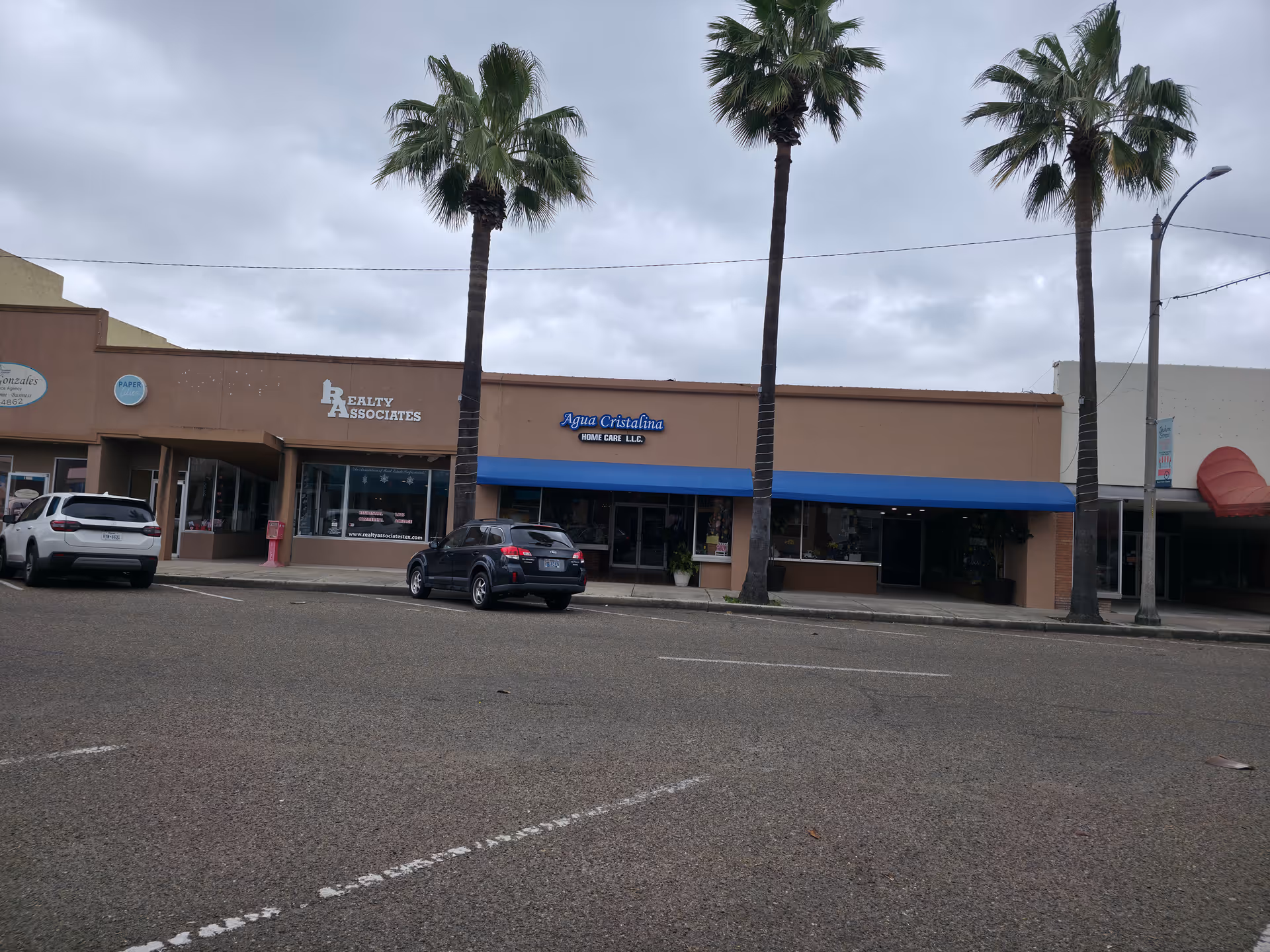 Exterior view of a strip mall with Agua Cristalina Home Care LLC sign and palm trees.