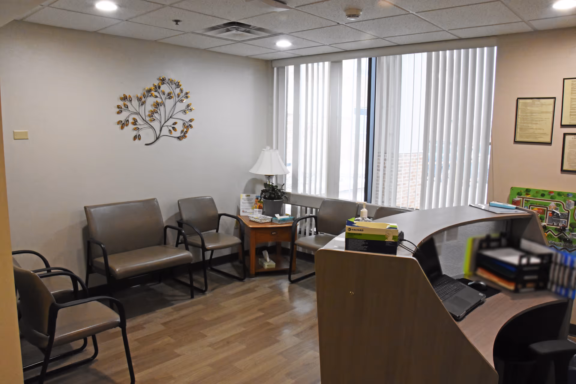 Interior waiting area with row of beige chairs, a curved front desk, and blinds.