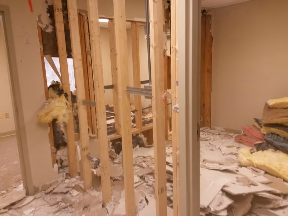 Construction in progress inside a facility with exposed studs, debris, and insulation on the floor.