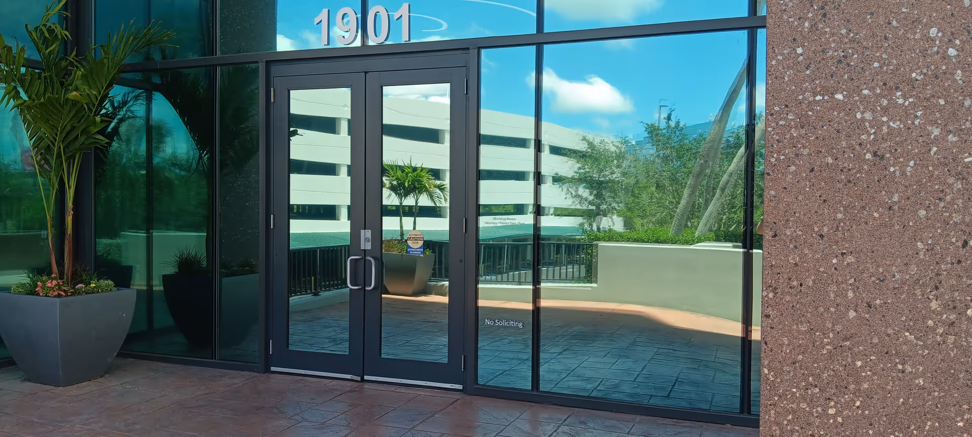 Glass entrance doors at Sunshine State Senior Care LLC, with planters outside and reflections.