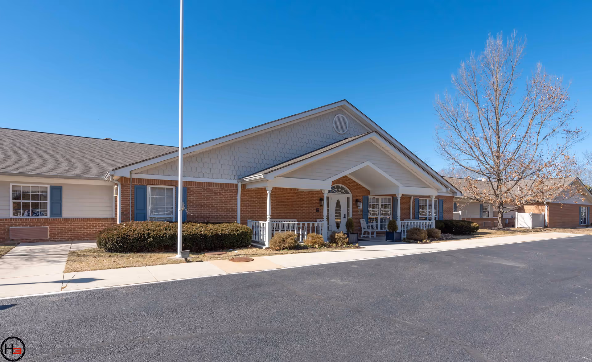 Single-story senior living facility with brick facade, covered entrance, parking lot, and bare trees.