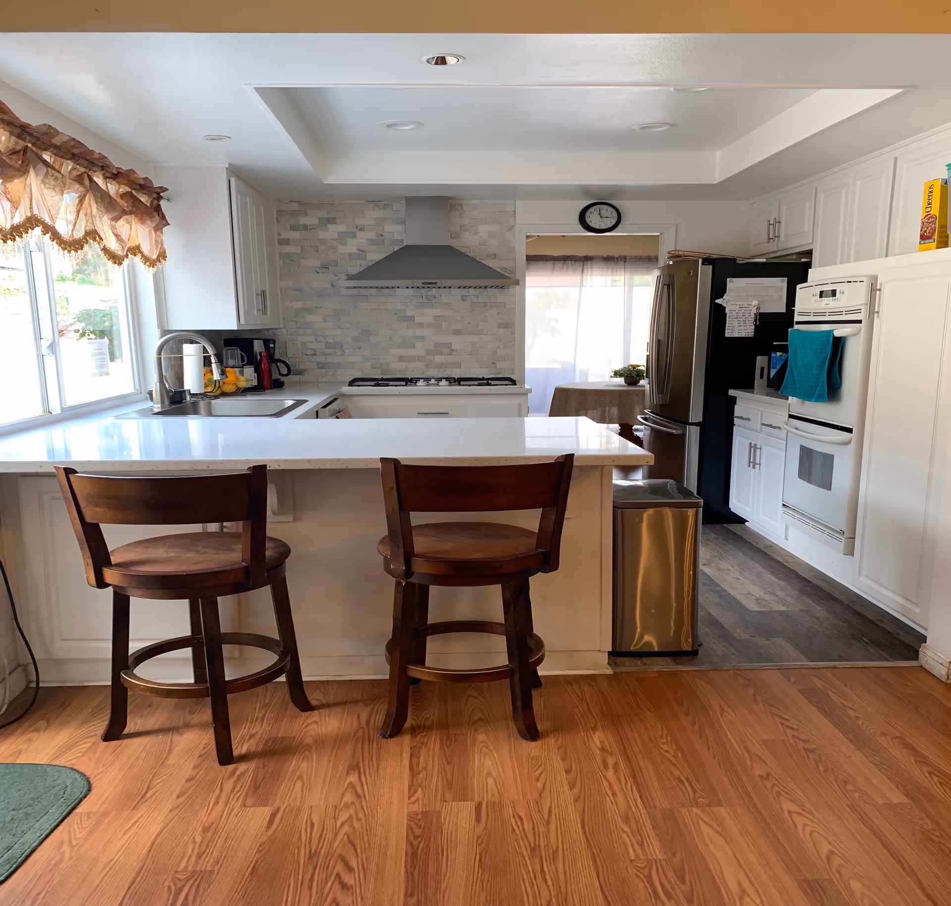 Bright kitchen with island seating, stainless appliances, white cabinets, and a tiled backsplash.