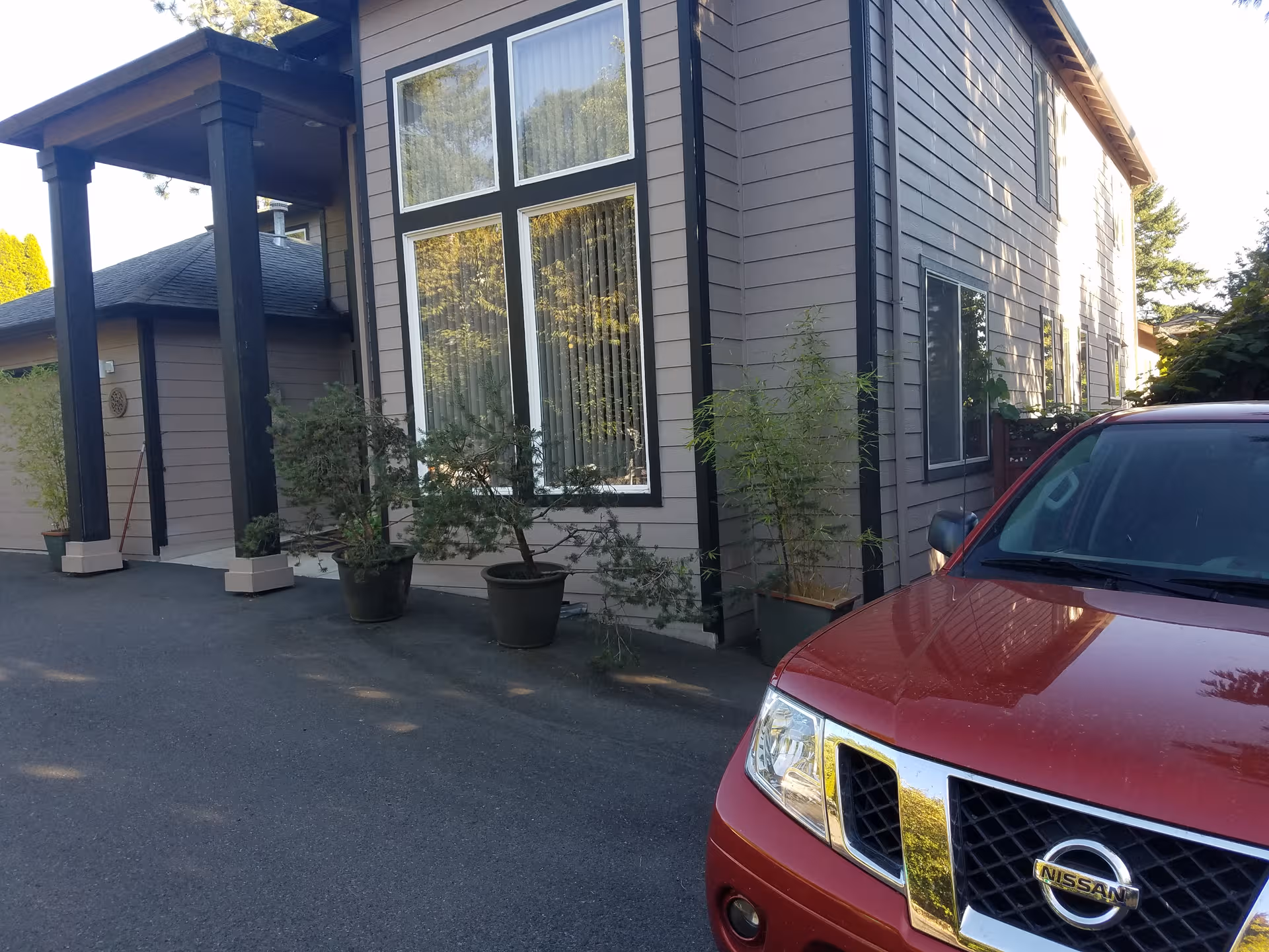 Front exterior of a grey building with large windows, potted plants, and a red car.