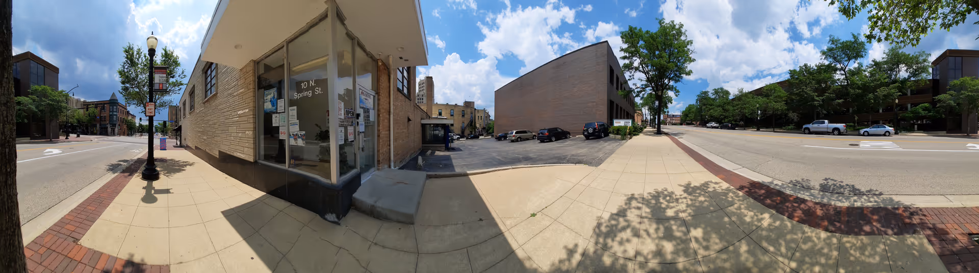 Panoramic exterior view of a building corner along sidewalk and street.