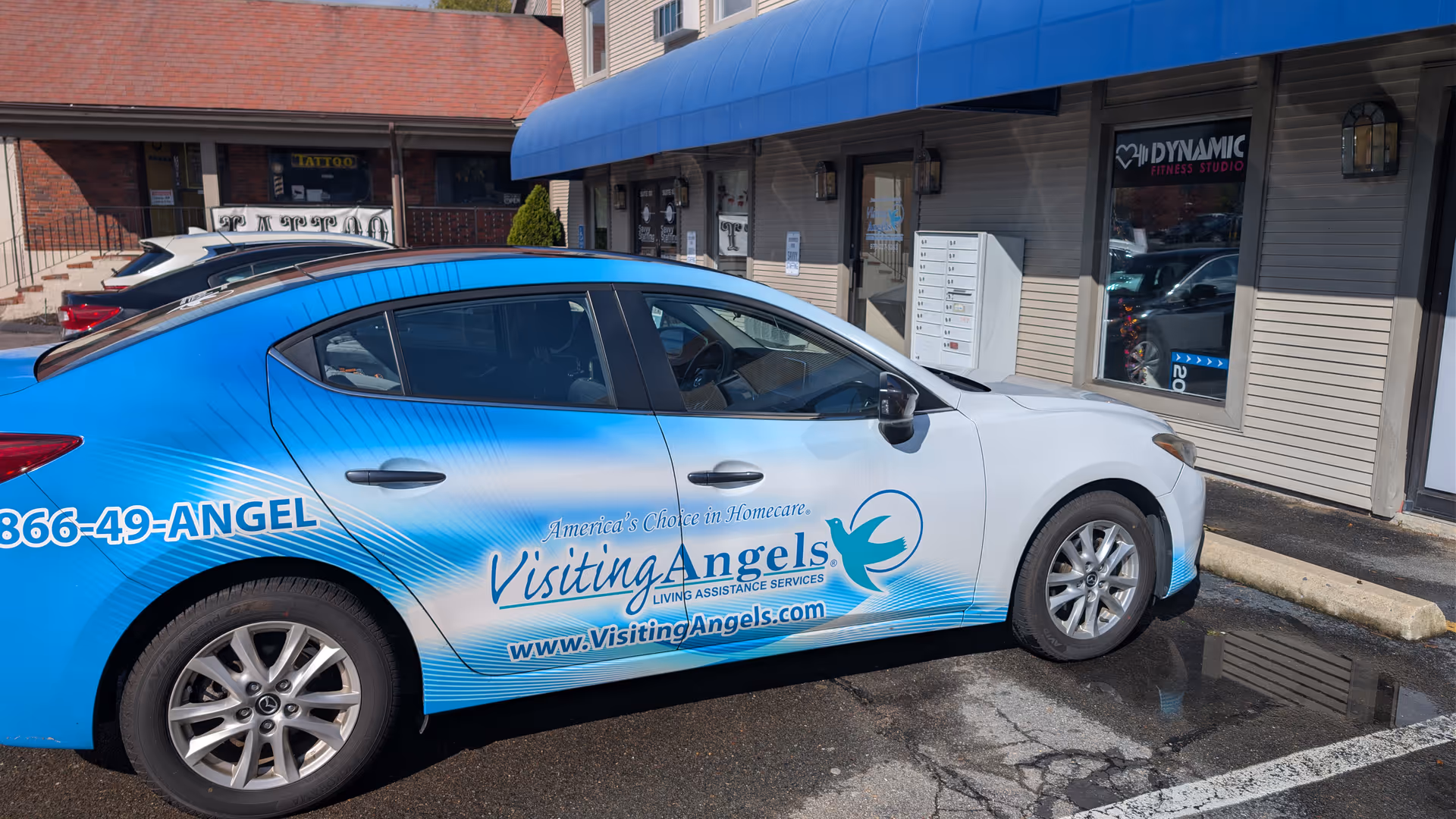 Blue Visiting Angels van parked outside a senior home care facility under a blue awning.