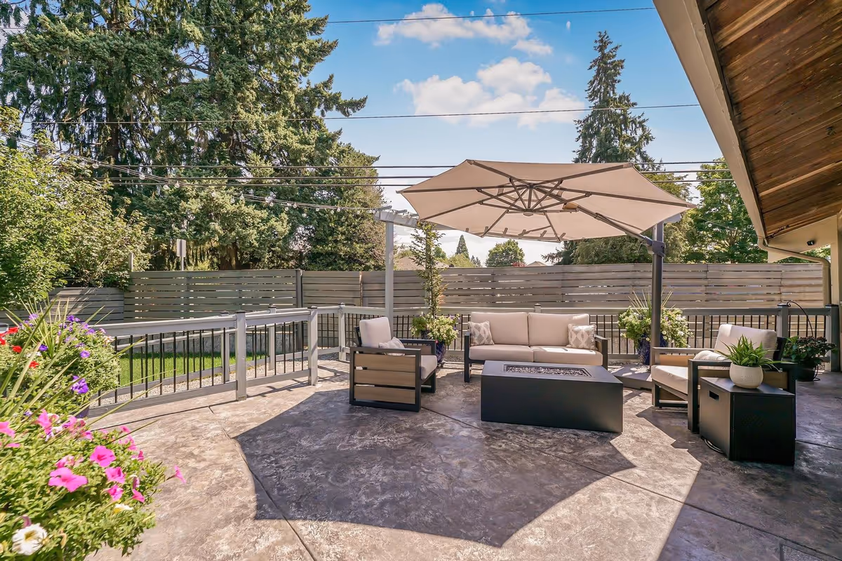 Outdoor patio with beige sectional seating, fire pit, umbrella, and potted plants.