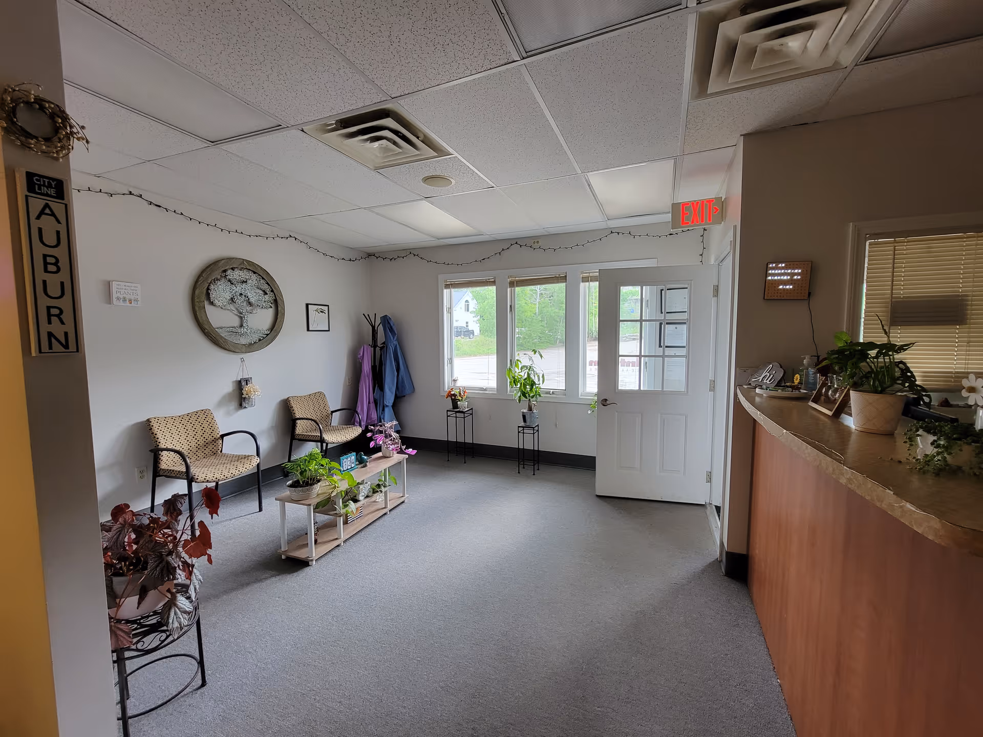 Lobby area with chairs, plants, a curved reception counter, and an exit door.