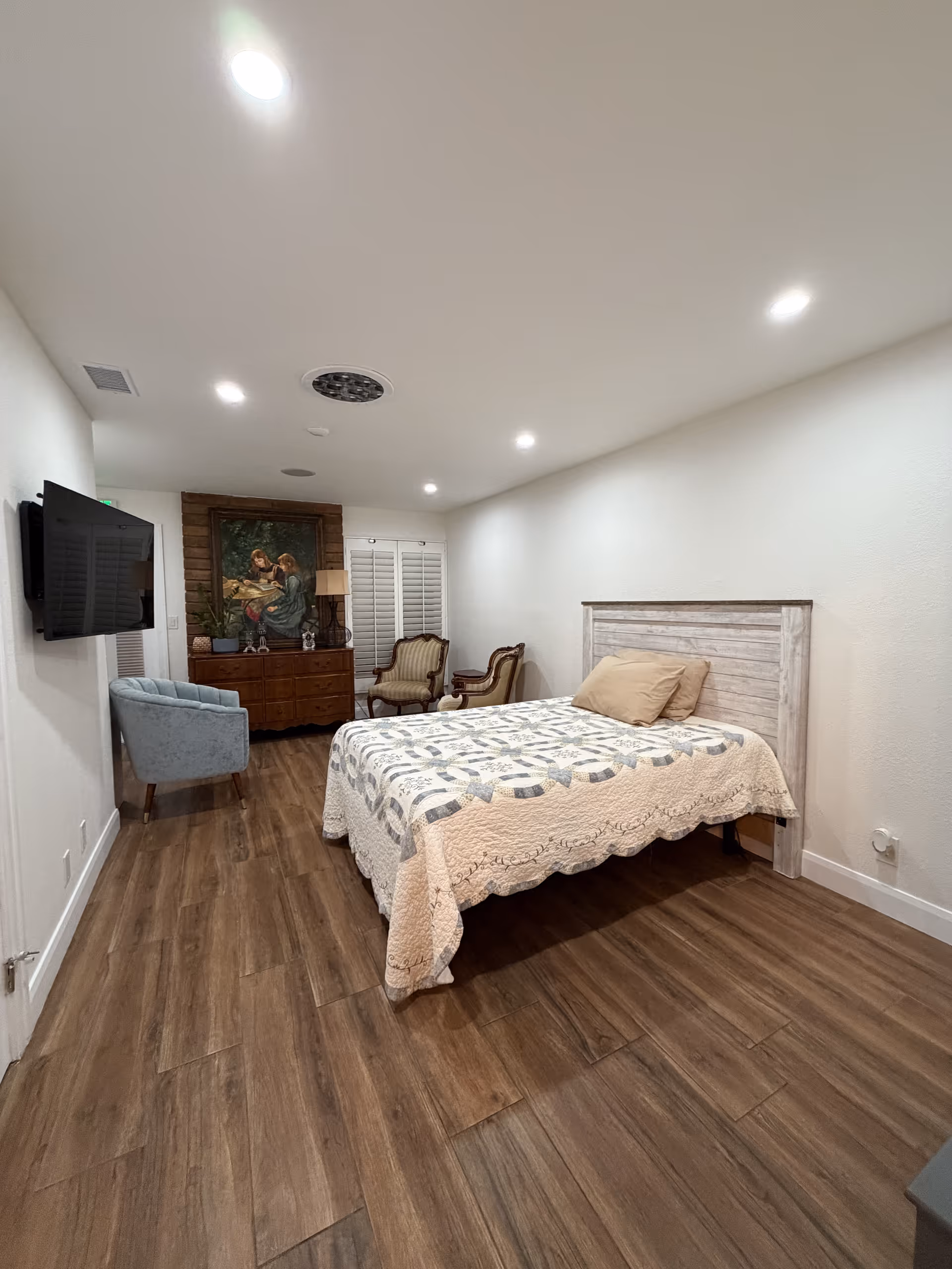 Bright senior living bedroom with a large bed, quilt, TV, and seating area.