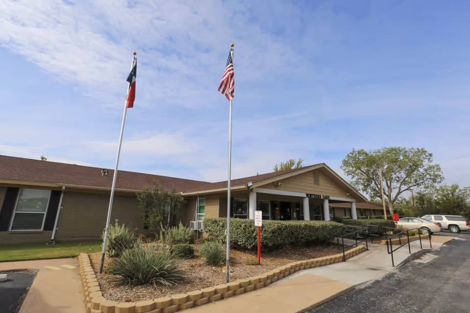 Exterior view of Northern Oaks facility with flags, ramp, hedges, and parked cars at the entrance.
