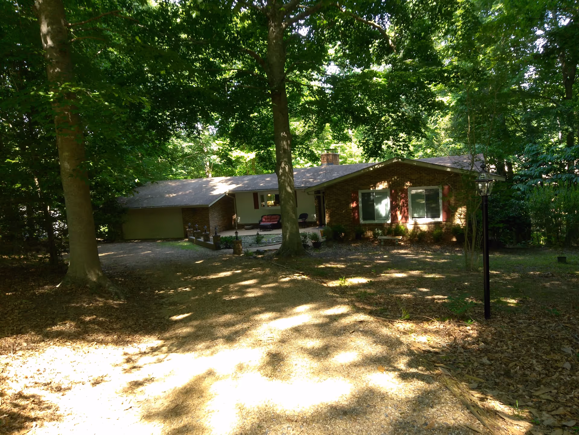 A single-story brick house in a wooded setting with driveway and front yard.