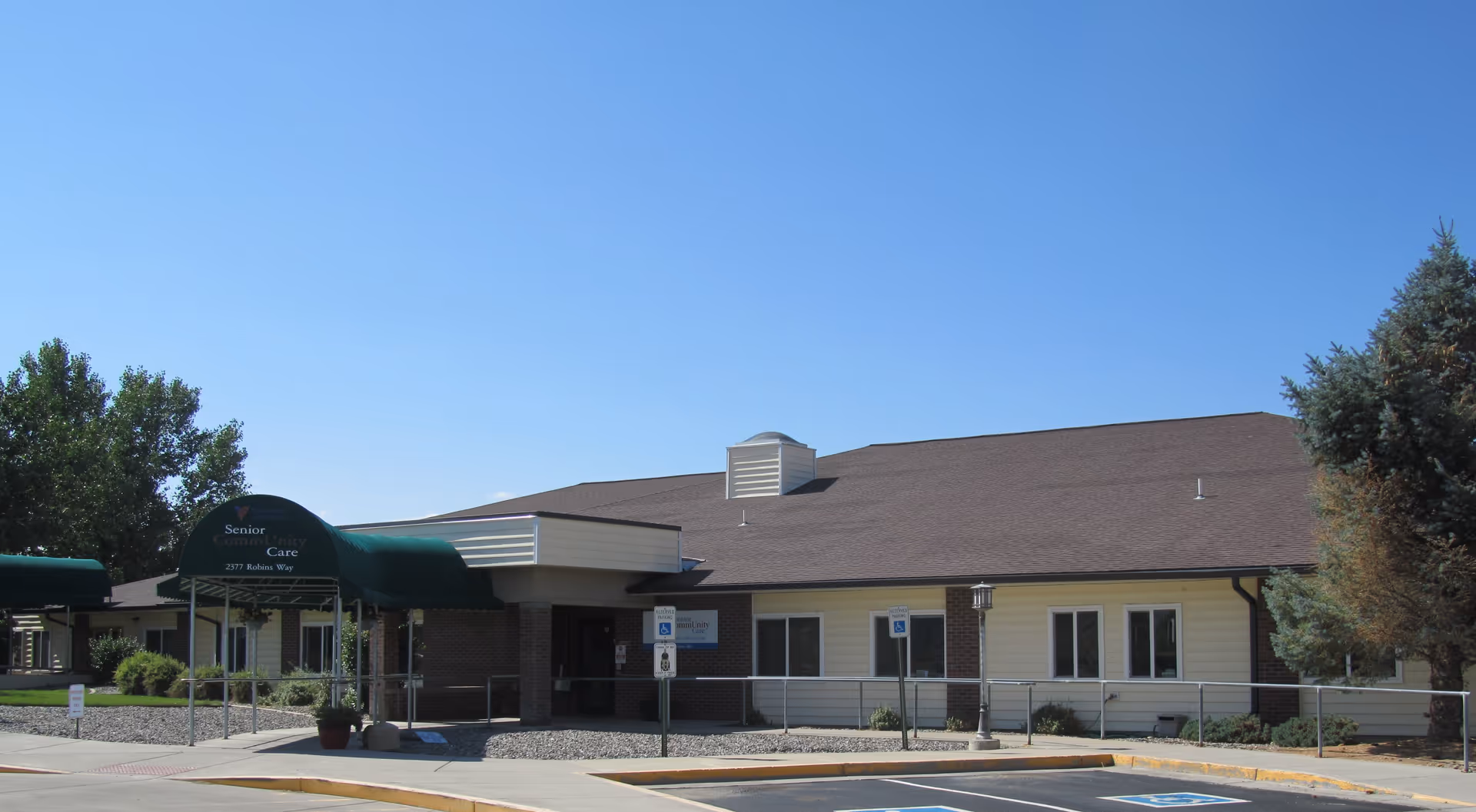 Single-story senior care building with a green canopy, ramp, and parking area.