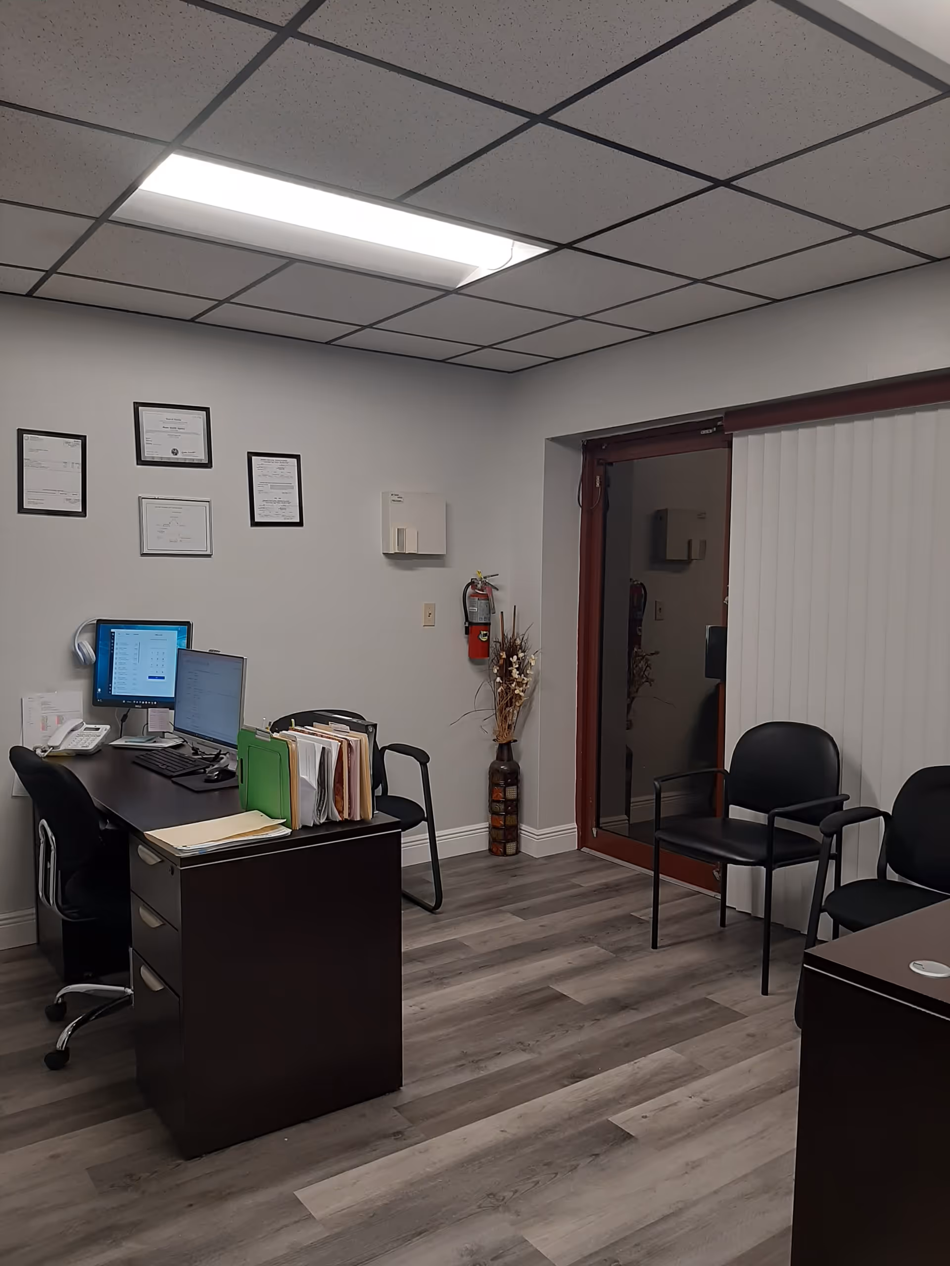 Office workspace with computer, paperwork, and chairs in a small reception area.