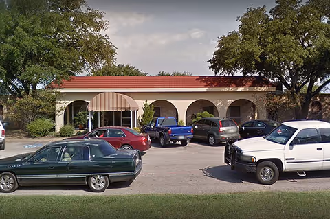 Front view of a building with arches and several parked cars in the parking lot.