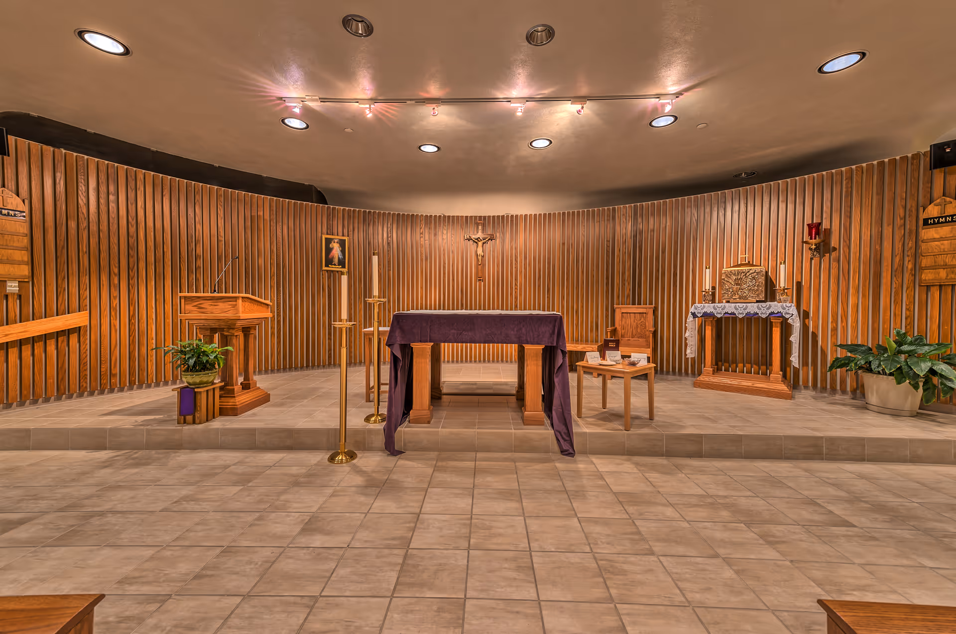 Hospital chapel altar area with crucifix, purple cloth, candles, and wood paneling.
