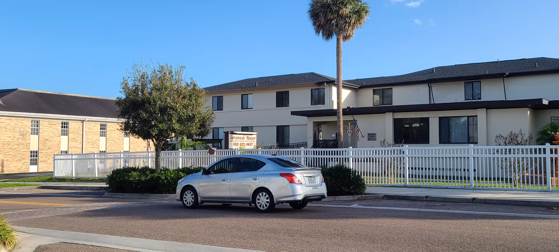 Exterior view of Savannah Court of Leesburg, a two-story senior living building with white fence.