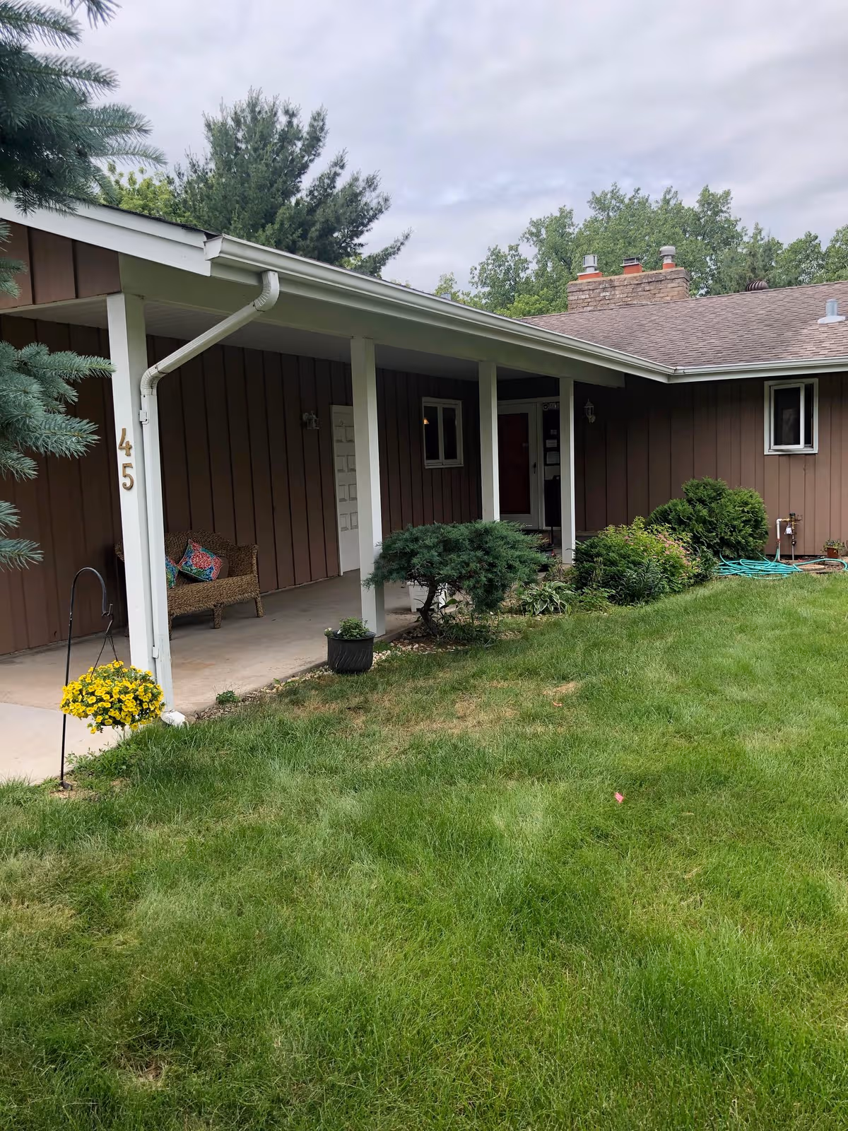 Brown single-story building with a covered front porch, green lawn, and shrubs.