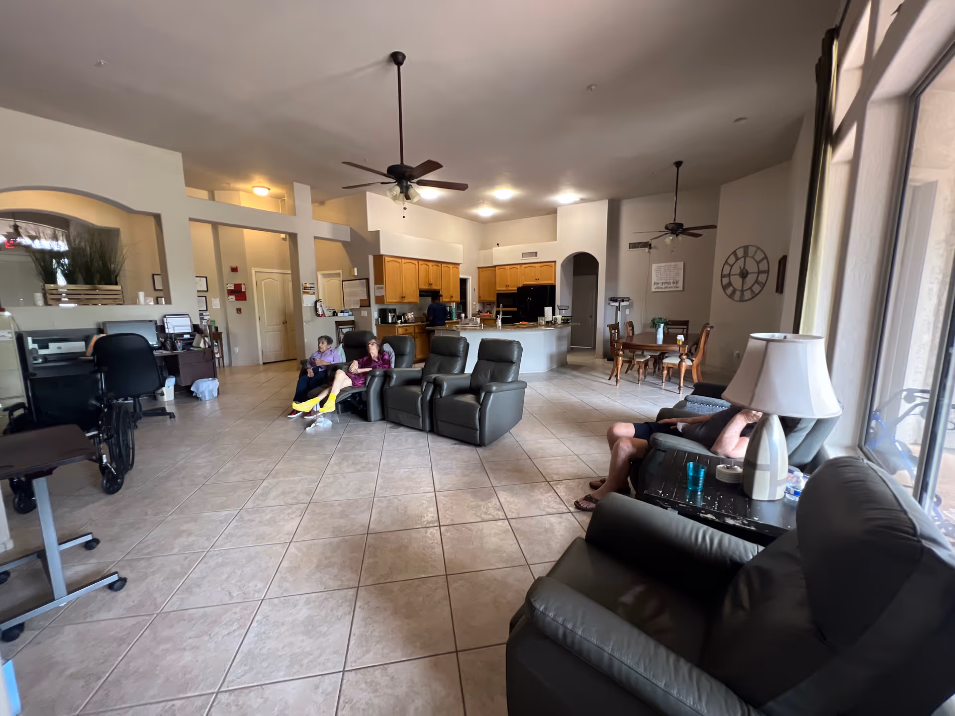 Spacious senior living common area with seating, a kitchen, and residents relaxing.