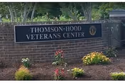 Brick sign for Thomson-Hood Veterans Center with flowering shrubs in front.
