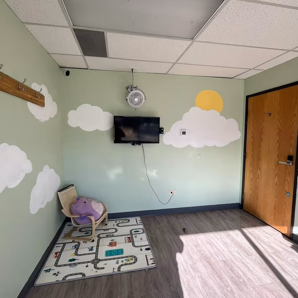 Room with cloud mural, small TV, chair, and road-pattern play mat on green walls