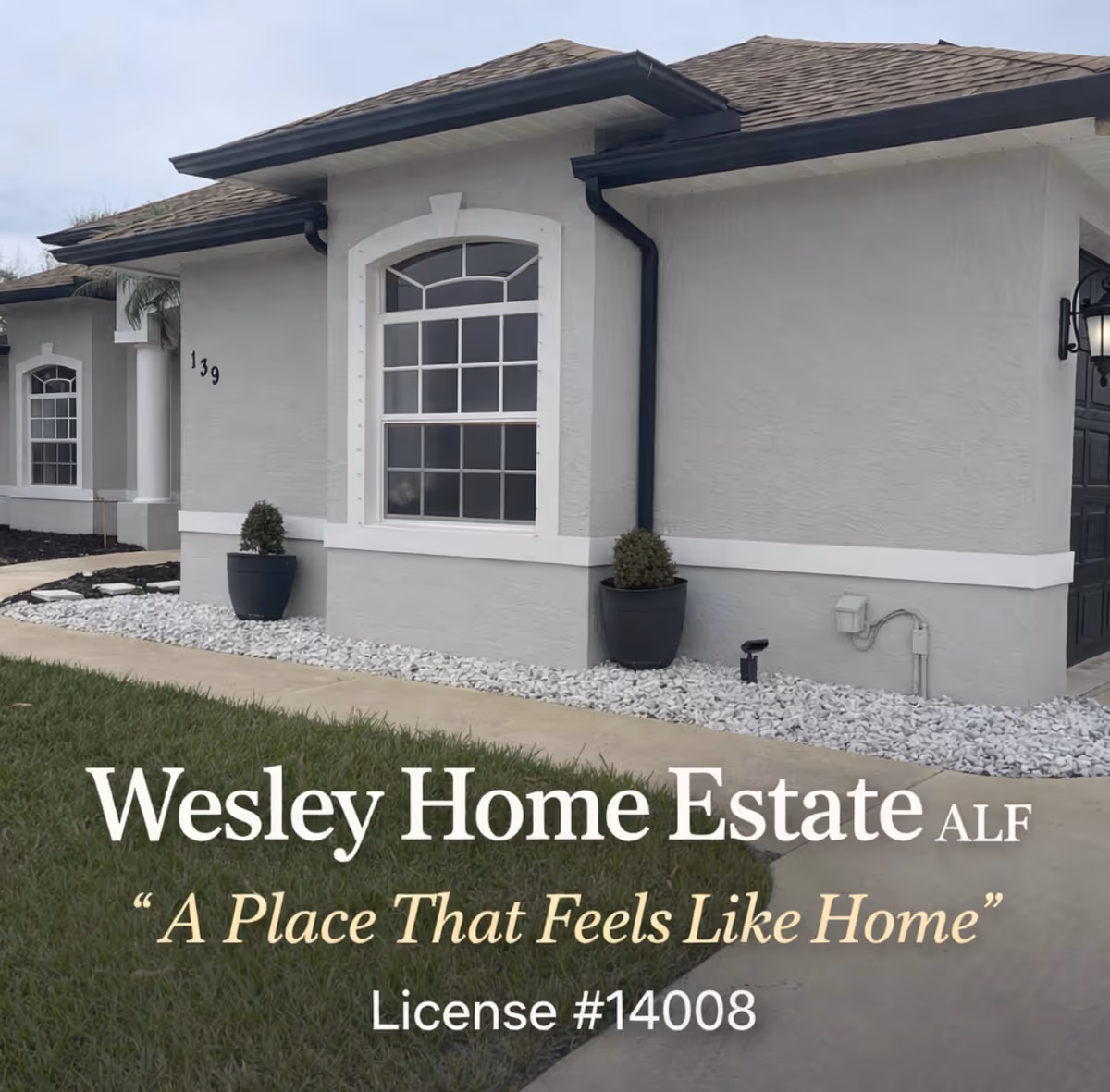A single-story gray senior living facility exterior with an arched window and landscaping.