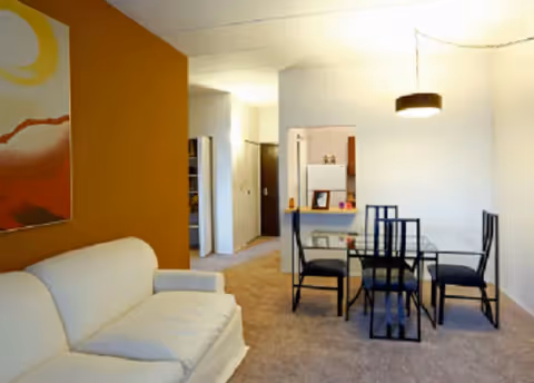 Bright living area with white sofa and dining table in a senior apartment common area.