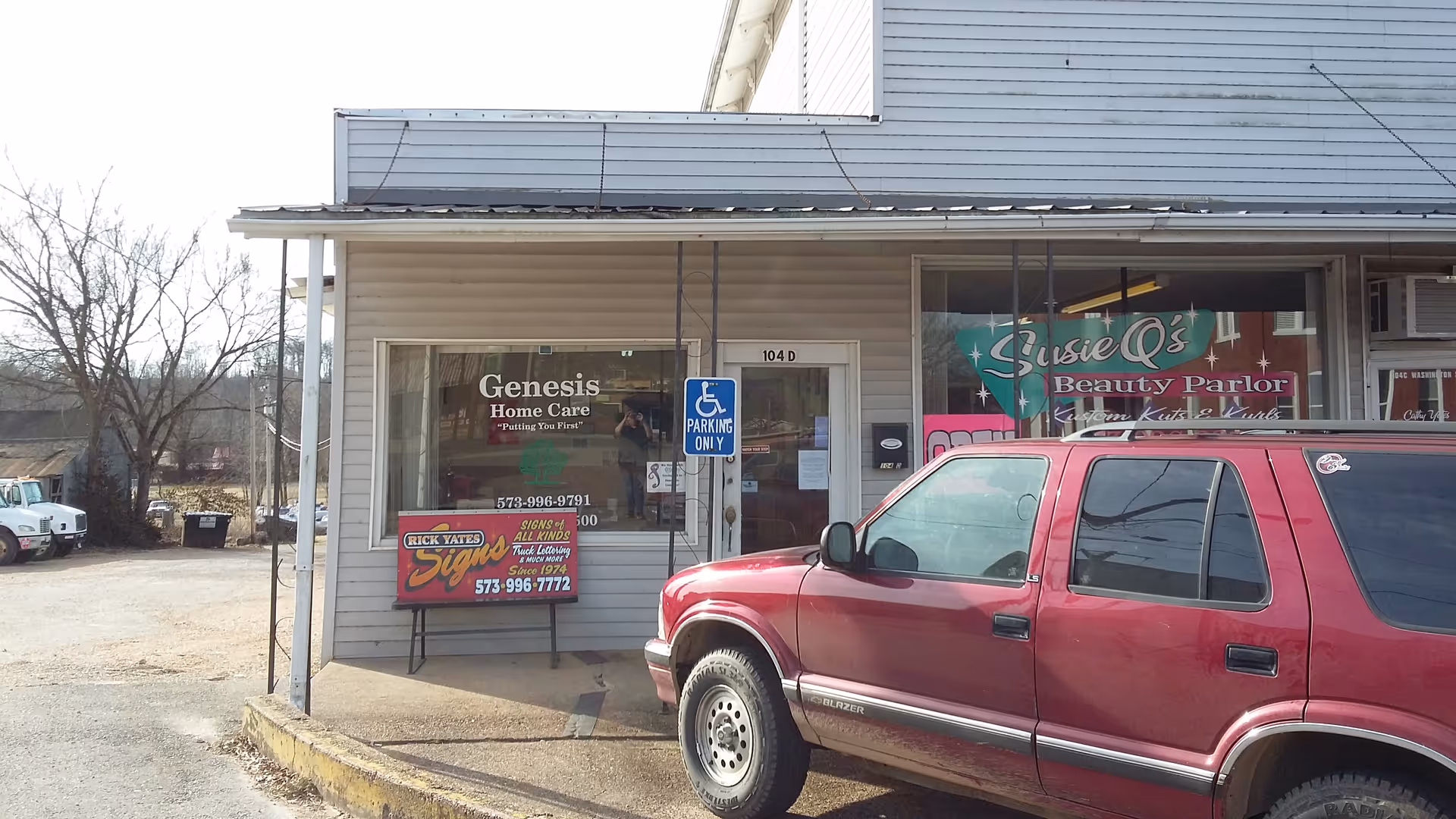 Exterior storefront with Genesis Home Care and Susie's Beauty Parlor, and a red SUV parked.