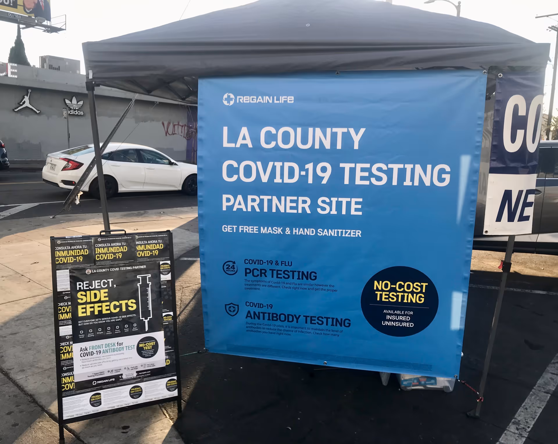 Blue COVID-19 testing banner under a tent in a parking lot.