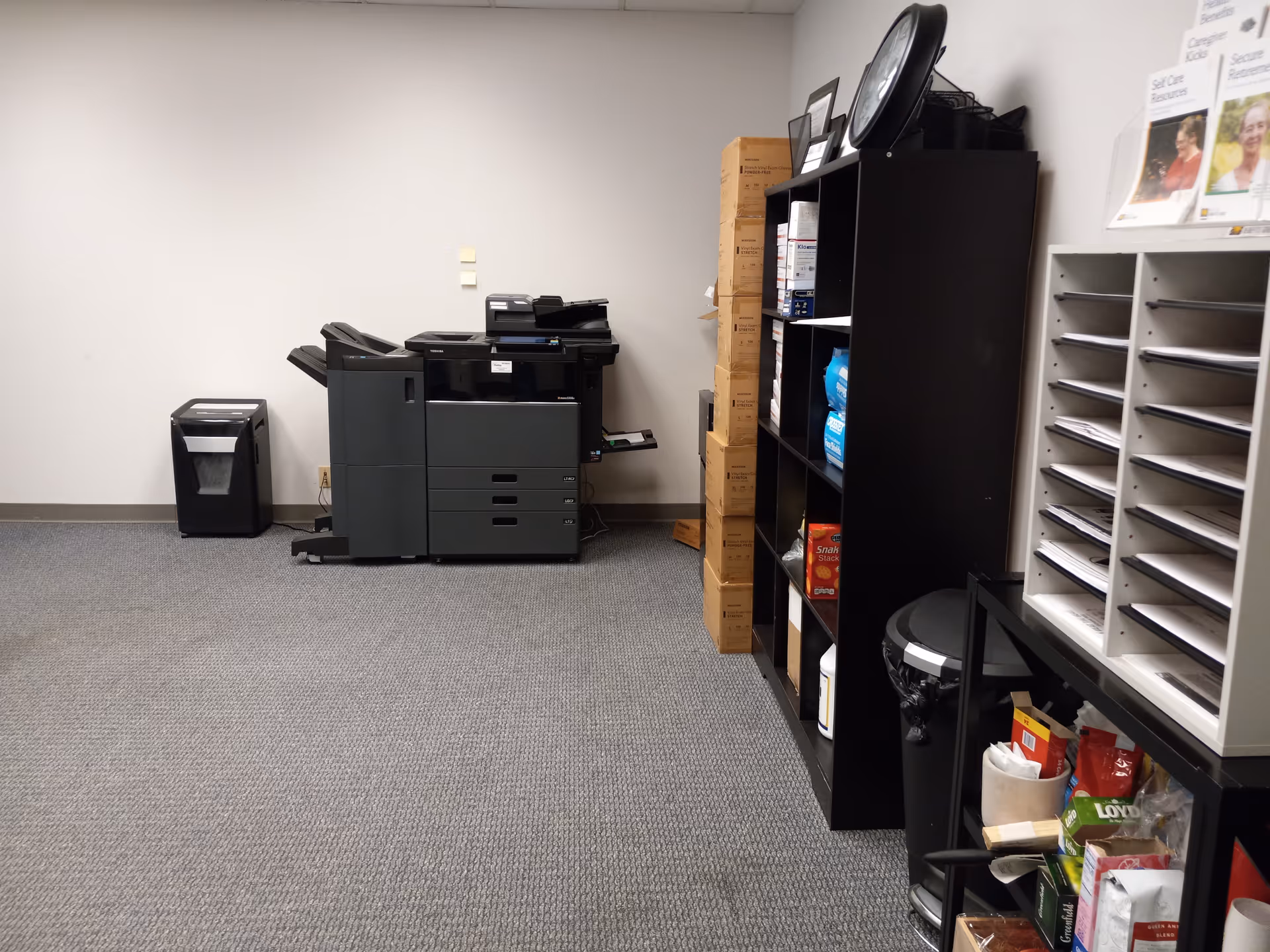 Office room with copier, shelves, stacked boxes, and mail-slot organizer.