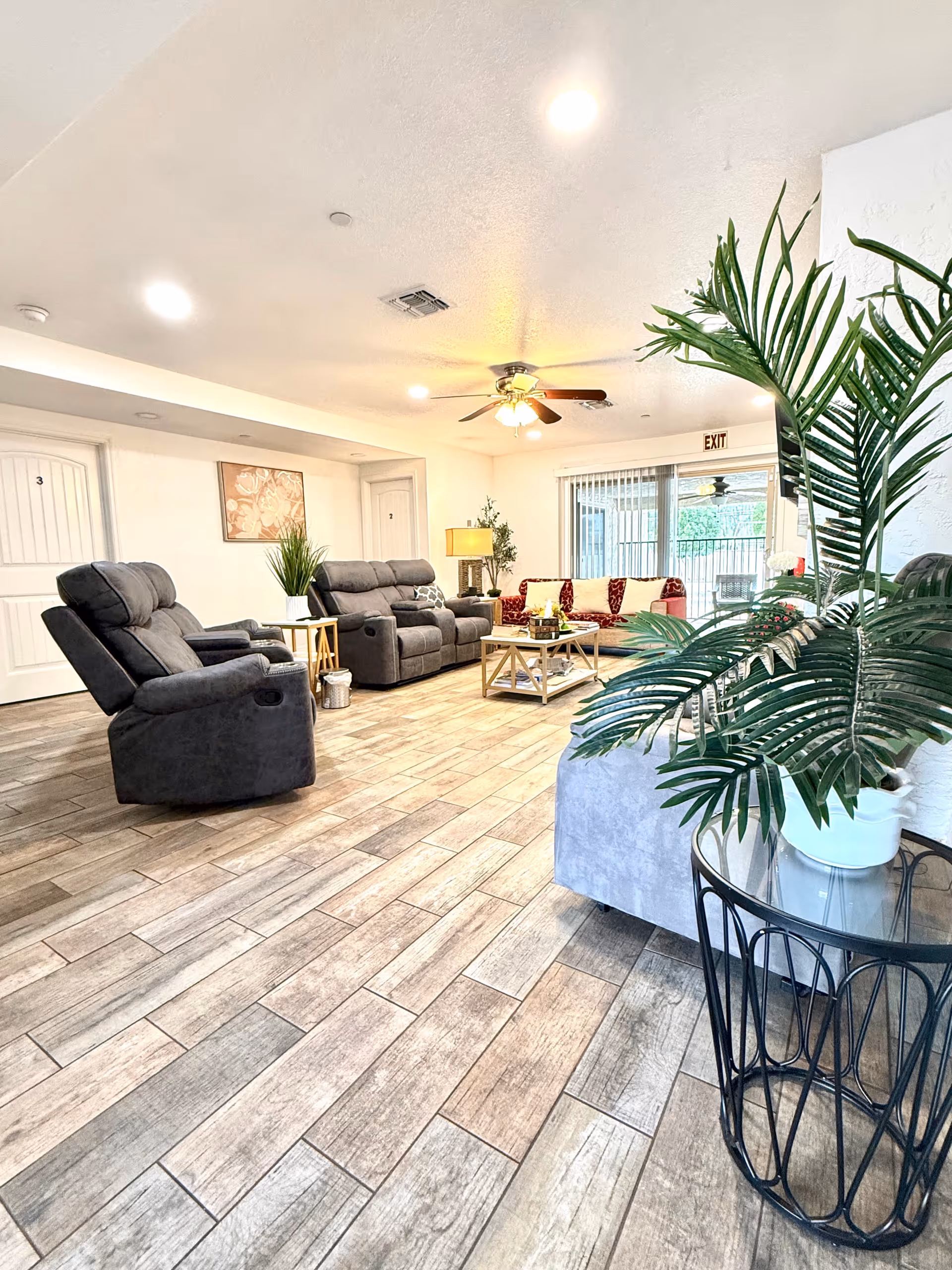 Bright communal living room with recliners, sofas, and potted plants.