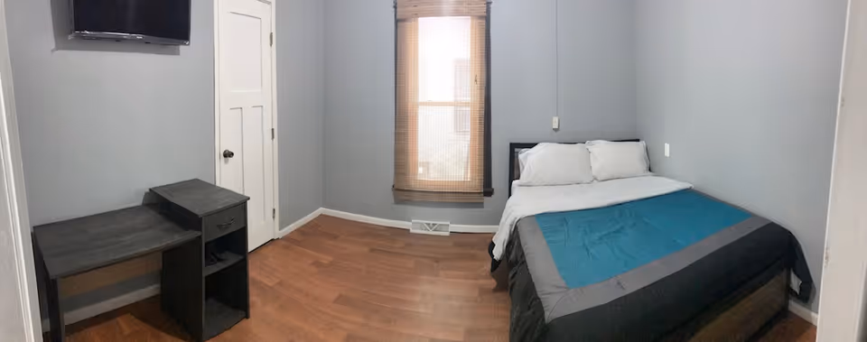 A compact Comfort Living bedroom with a bed, desk, window, and wall-mounted TV.
