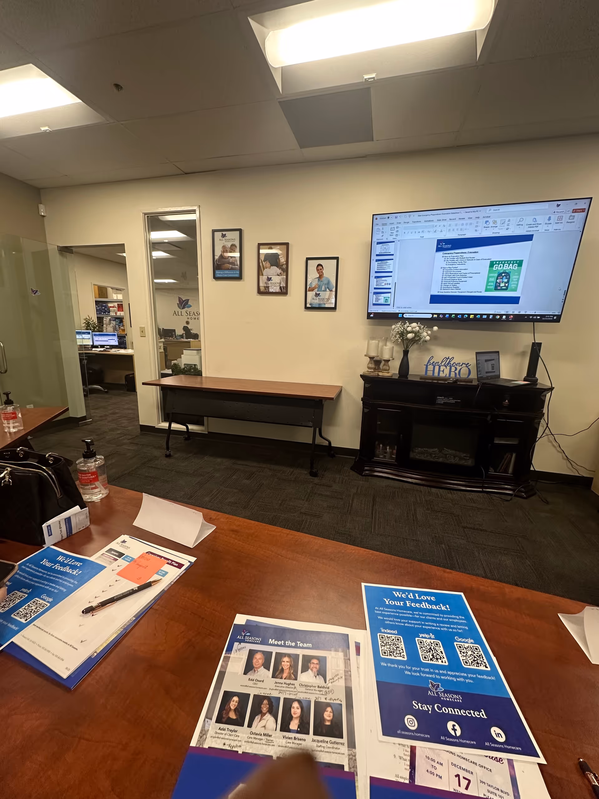 All Seasons Homecare office area featuring brochures, a large mounted screen, and a reception-style console.