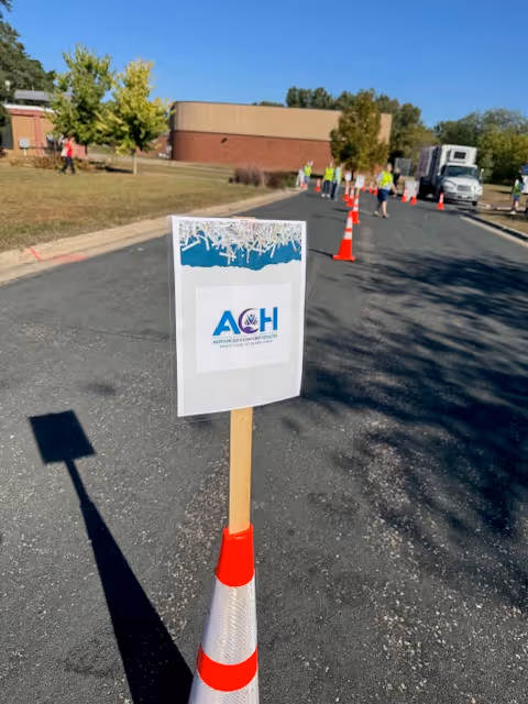 Facility exterior with orange cones, a sign, and staff in high-visibility vests outside.