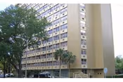 Exterior view of a tall beige senior living building with surrounding trees.