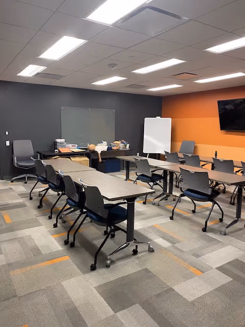 An empty meeting room in a senior facility with desks, chairs, whiteboard, and a TV.