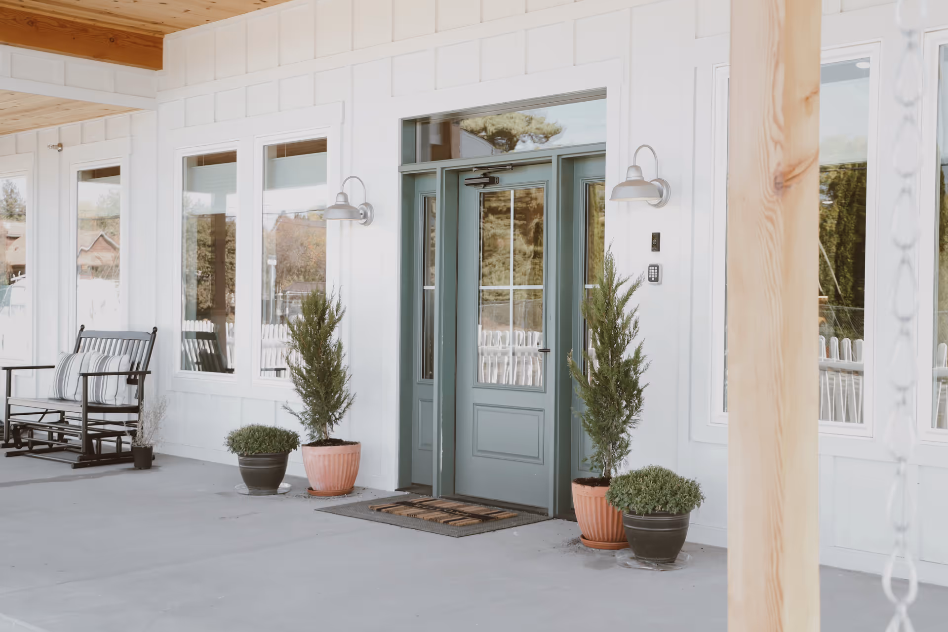 Light exterior of Hill House Memory Care entrance with a blue-green door and potted plants