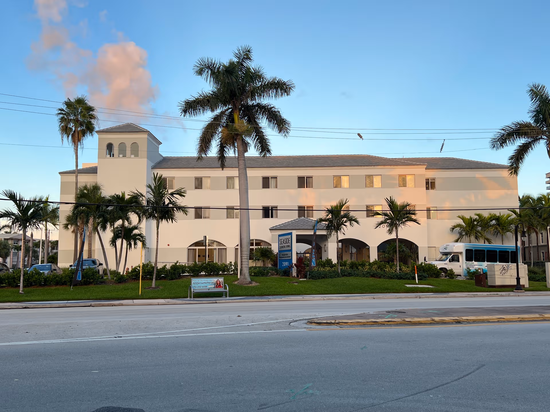 Front view of Seaside Hallandale Beach Senior Living building with palm trees and a bus.