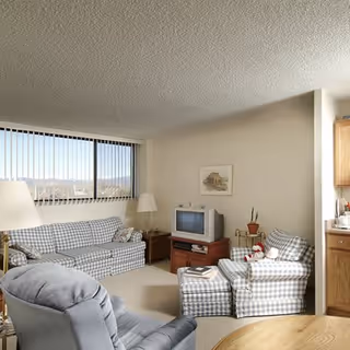 Sunlit living room in a senior facility with checkered sofas, TV, and a kitchenette.
