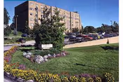 A brick assisted-living building with a manicured lawn and colorful flower beds in front.