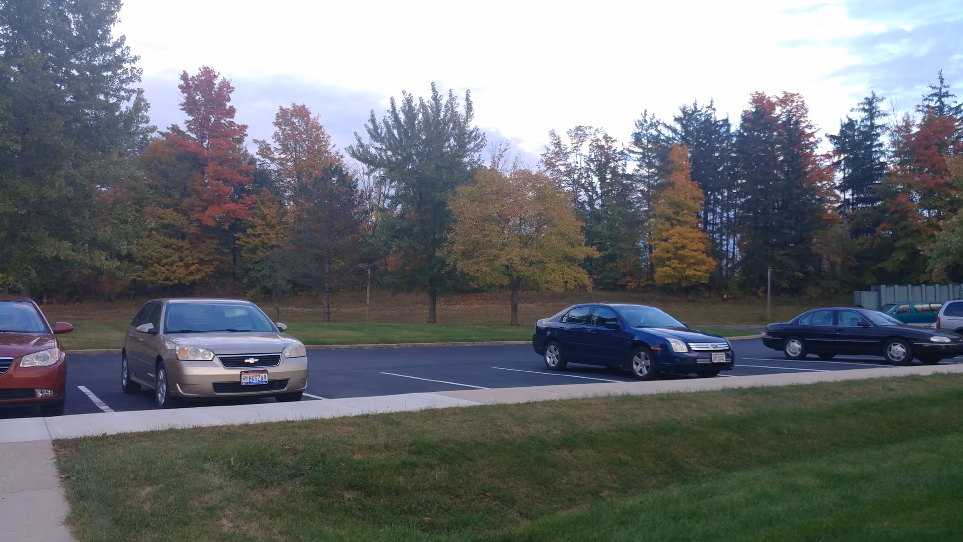 Parking lot with several cars and autumn-colored trees in the background.