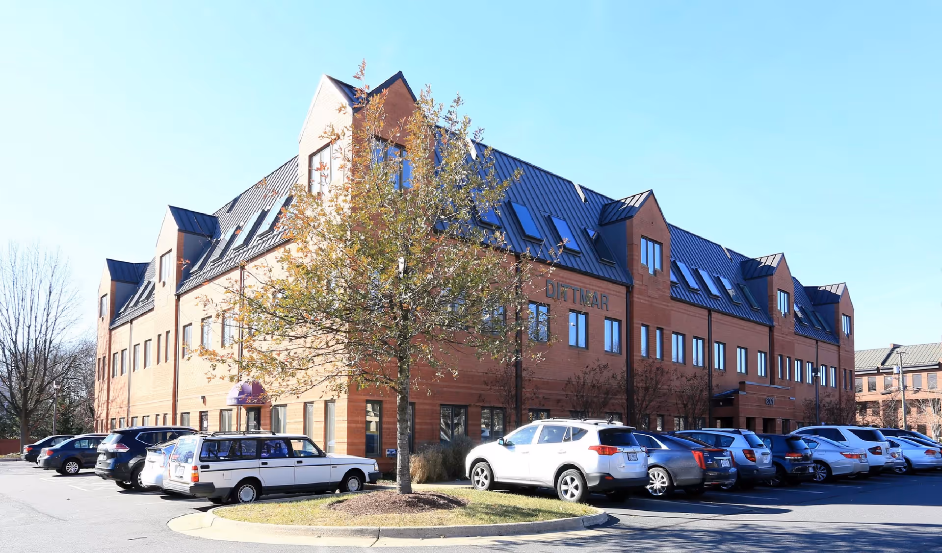 Brick senior living building with gabled roofs and a parking lot in front.