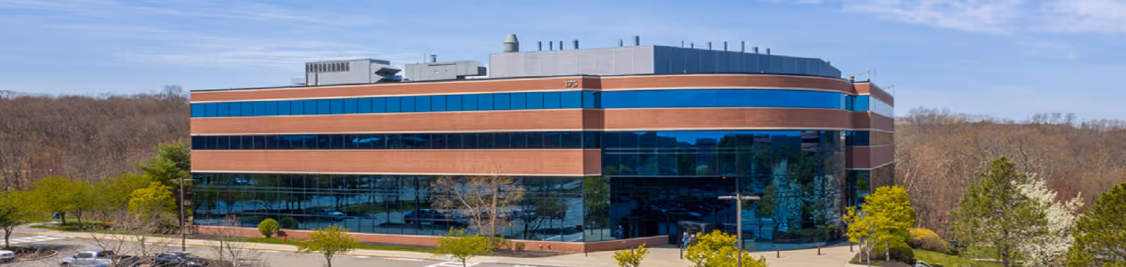 A modern brick-and-glass building with a curved facade, surrounded by trees and a parking lot.