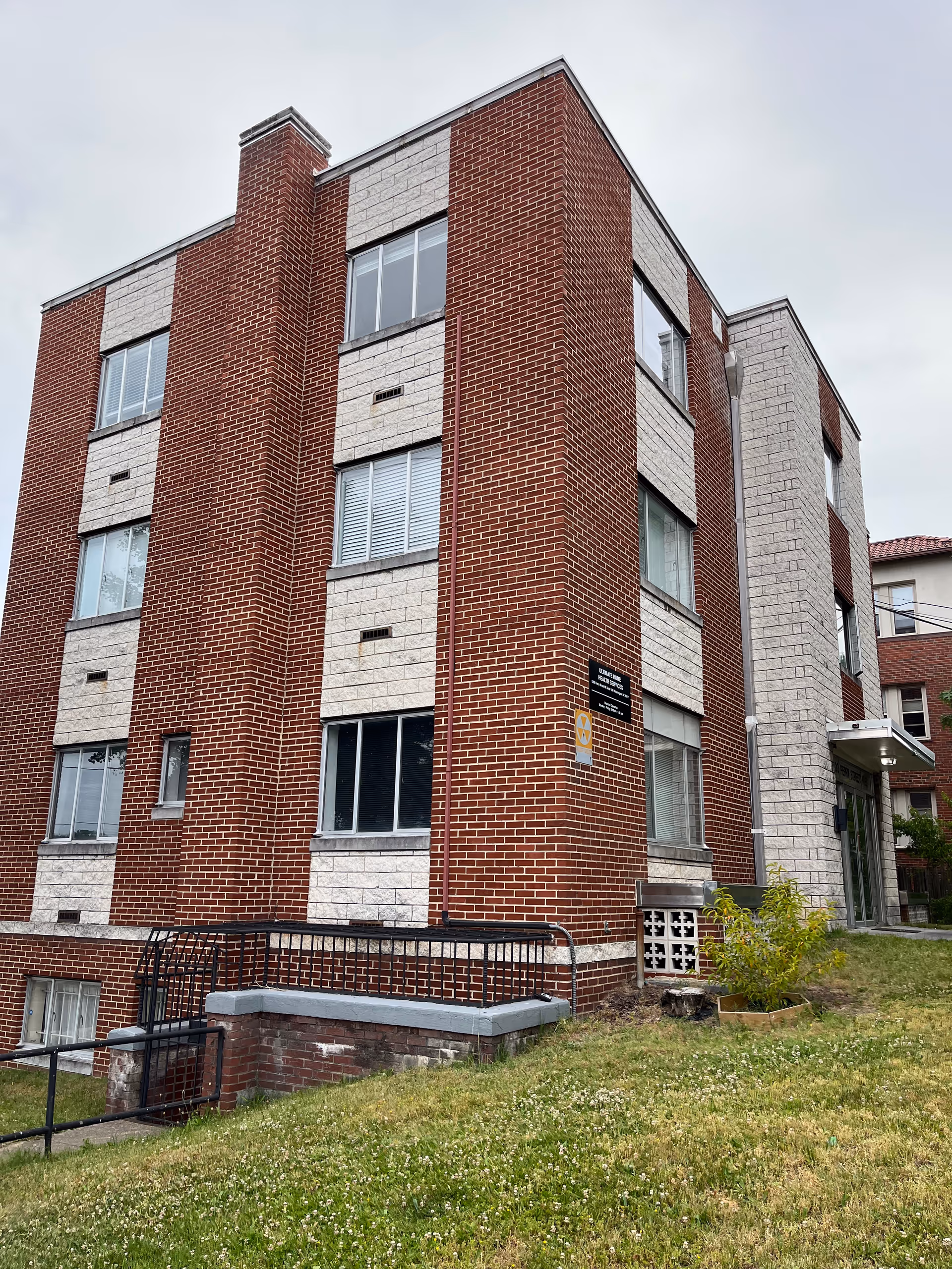 Brick, multi-story senior living facility exterior with tall windows and grassy foreground.