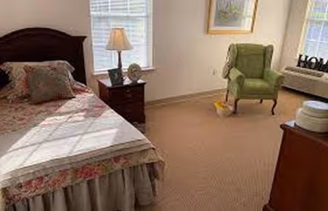 Bedroom in Woodlawn Haven Rest Home with bed, chair, and lamp.