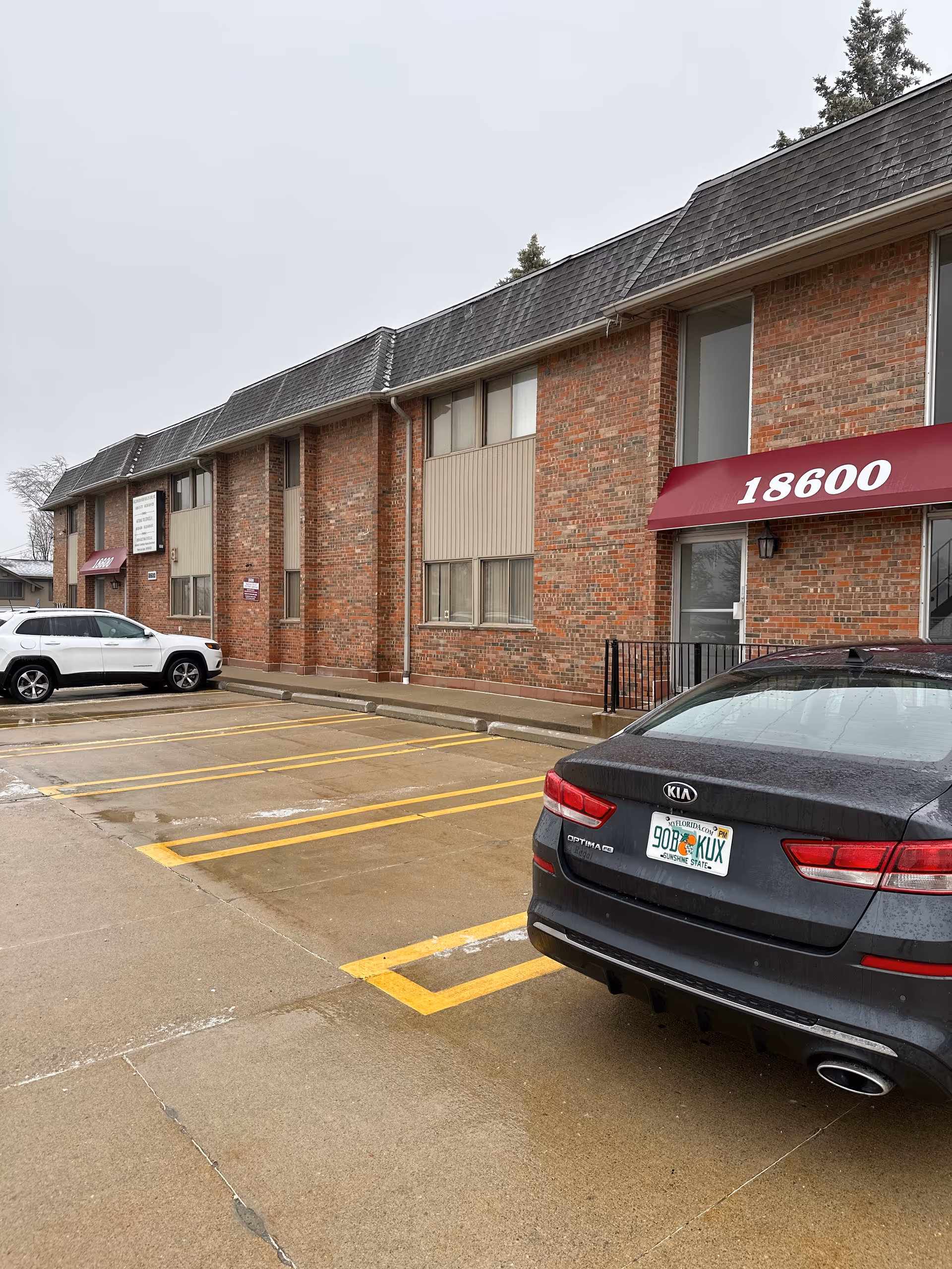Brick senior living facility exterior with parked cars and a maroon storefront awning.