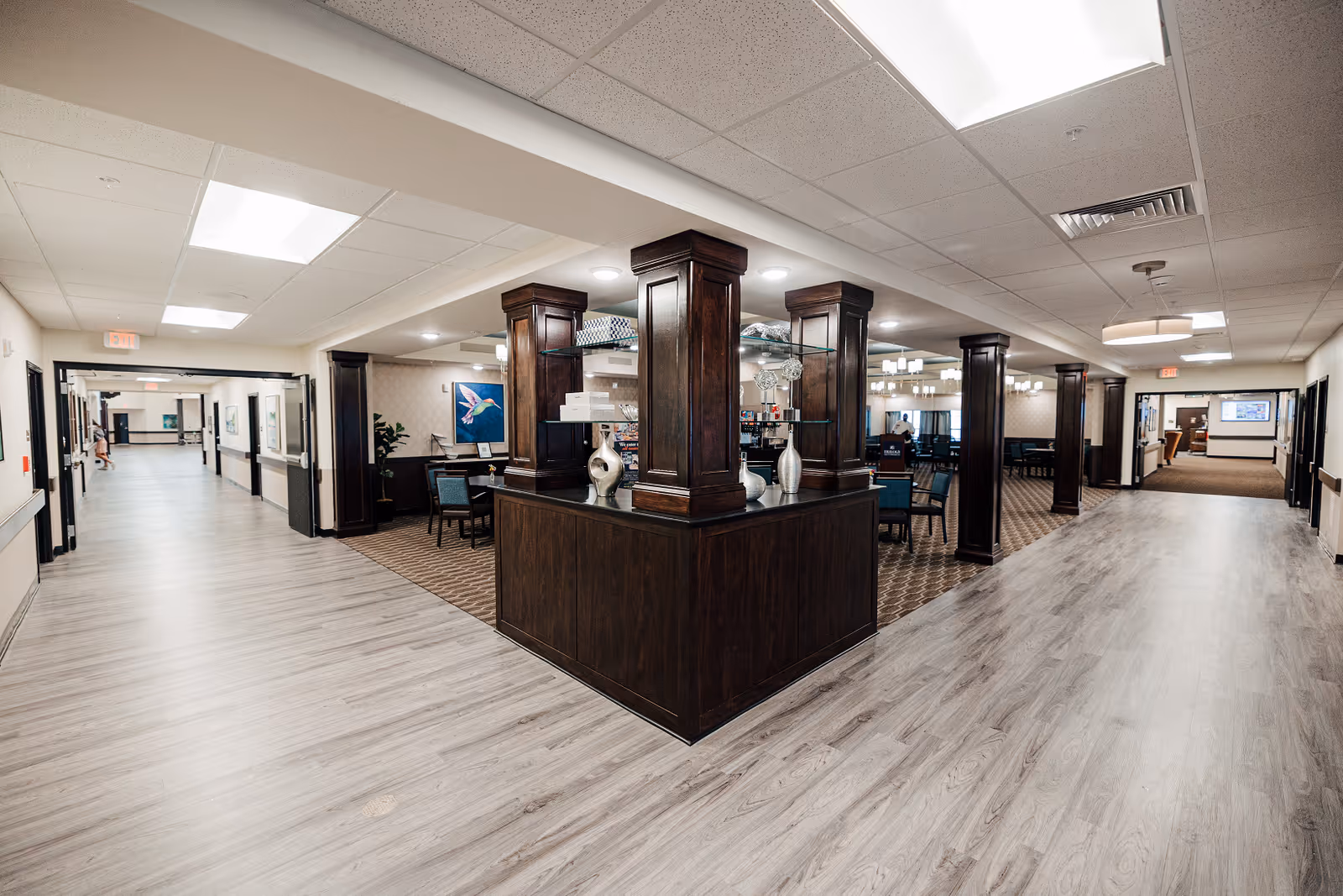 Spacious senior living lobby with dark wood columns, seating areas, and bright overhead lighting.