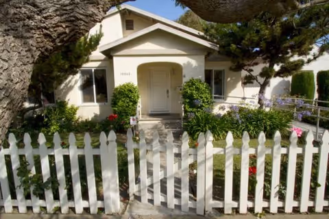 Front view of a single-story residential care home with a white picket fence.