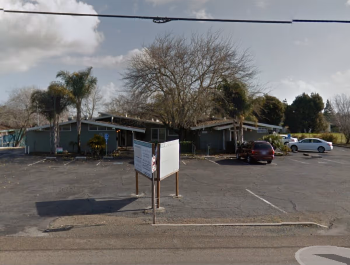 A single-story senior care facility exterior with parking lot and a signboard.