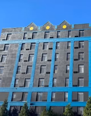 Tall gray building with blue bands and yellow circular accents under a clear sky.